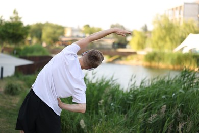 Photo of Sportsman in headphones doing morning exercise outdoors, back view