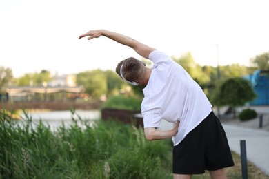 Photo of Sportsman in headphones doing morning exercise outdoors, back view