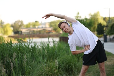 Photo of Smiling sportsman in headphones doing morning exercise outdoors