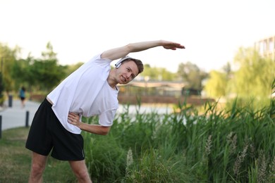 Photo of Smiling sportsman in headphones doing morning exercise outdoors