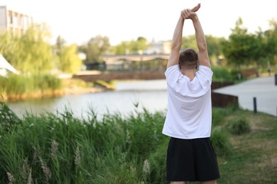 Photo of Sportsman in headphones doing morning exercise outdoors, back view. Space for text