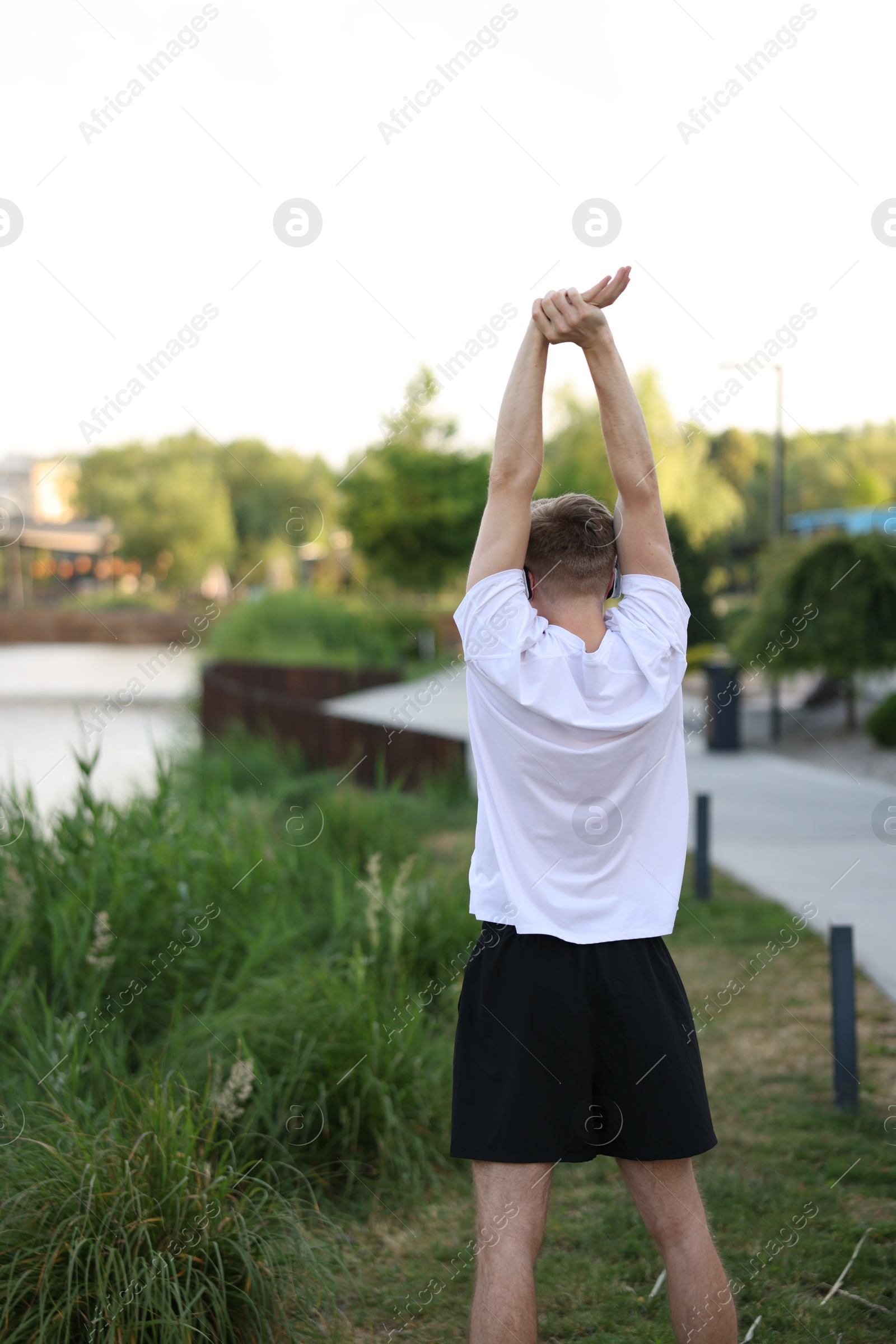 Sportsman in headphones doing morning exercise outdoors, back view Photo of Sportsman in headphones doing morning exercise outdoors, back view