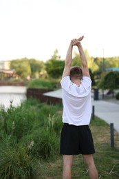 Photo of Sportsman in headphones doing morning exercise outdoors, back view