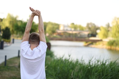 Photo of Sportsman in headphones doing morning exercise outdoors, back view