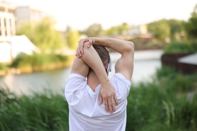Photo of Sportsman in headphones doing morning exercise outdoors, back view