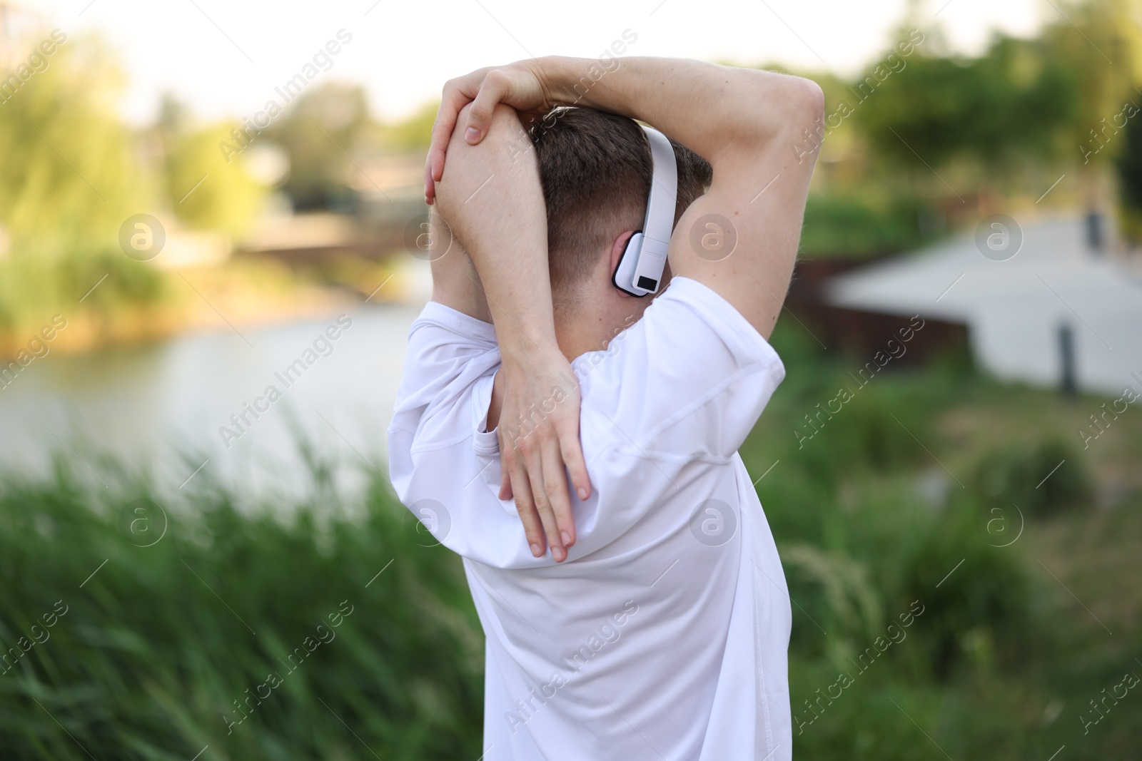 Sportsman in headphones doing morning exercise outdoors, back view Photo of Sportsman in headphones doing morning exercise outdoors, back view