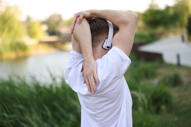 Photo of Sportsman in headphones doing morning exercise outdoors, back view