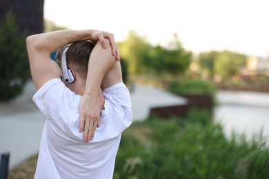 Photo of Sportsman in headphones doing morning exercise outdoors, back view