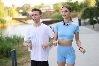 Photo of Happy couple with bottle of water running outdoors. Morning exercise