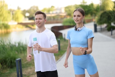 Photo of Happy couple with bottle of water running outdoors. Morning exercise