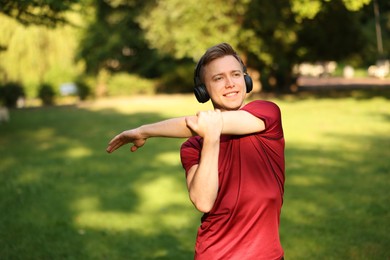 Photo of Smiling sportsman in headphones doing morning exercise outdoors