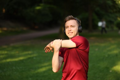 Photo of Smiling sportsman in headphones doing morning exercise outdoors