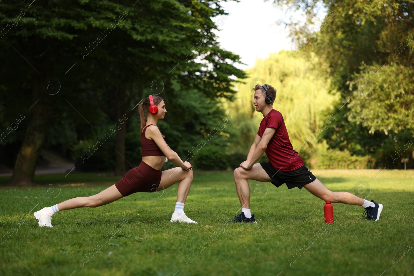 Happy couple in headphones doing morning exercises in park Photo of Happy couple in headphones doing morning exercises in park