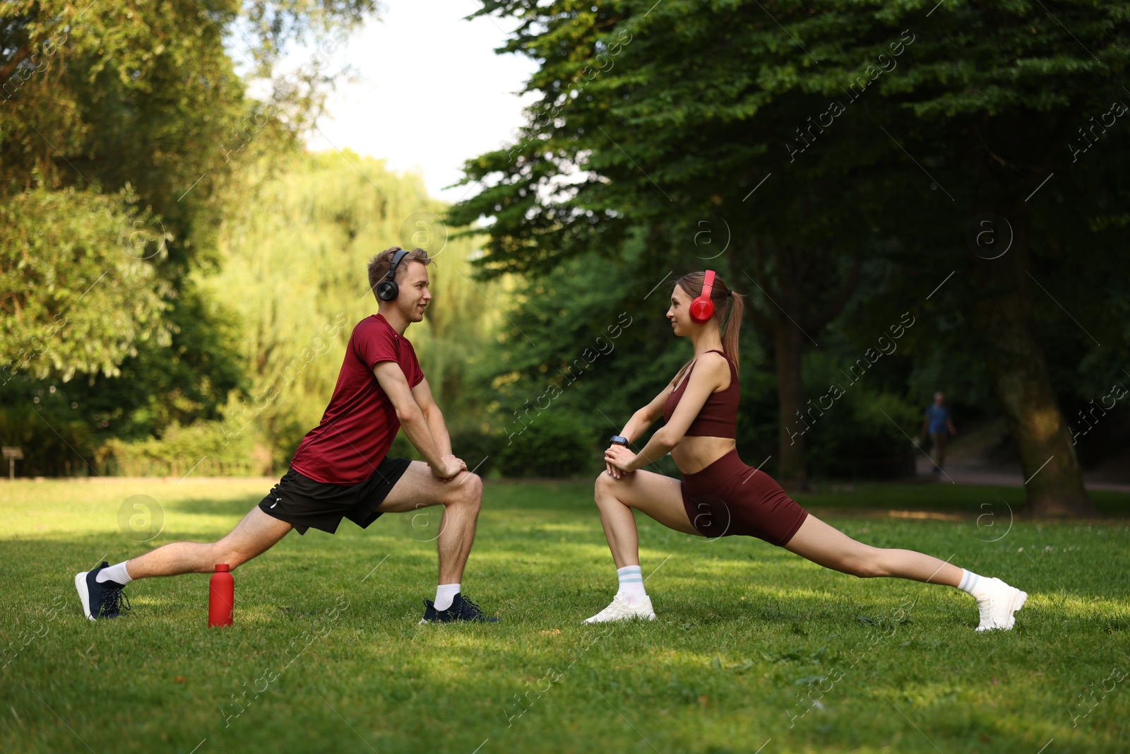 Happy couple in headphones doing morning exercises in park Photo of Happy couple in headphones doing morning exercises in park