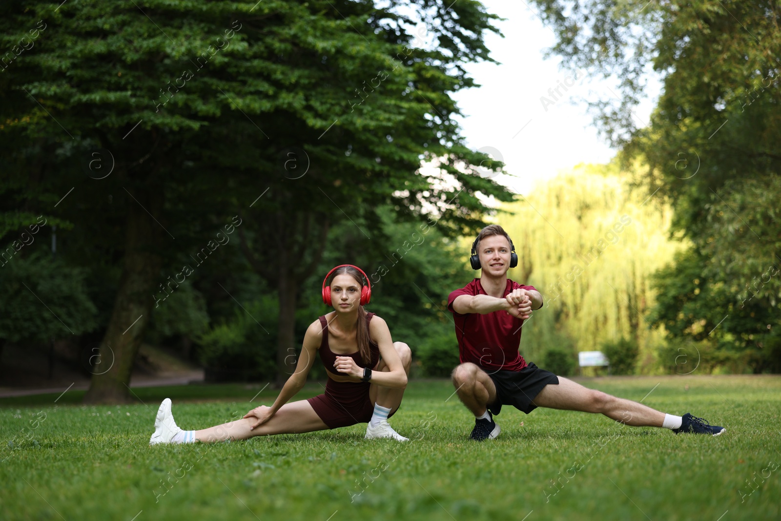 Happy couple in headphones doing morning exercises in park Photo of Happy couple in headphones doing morning exercises in park