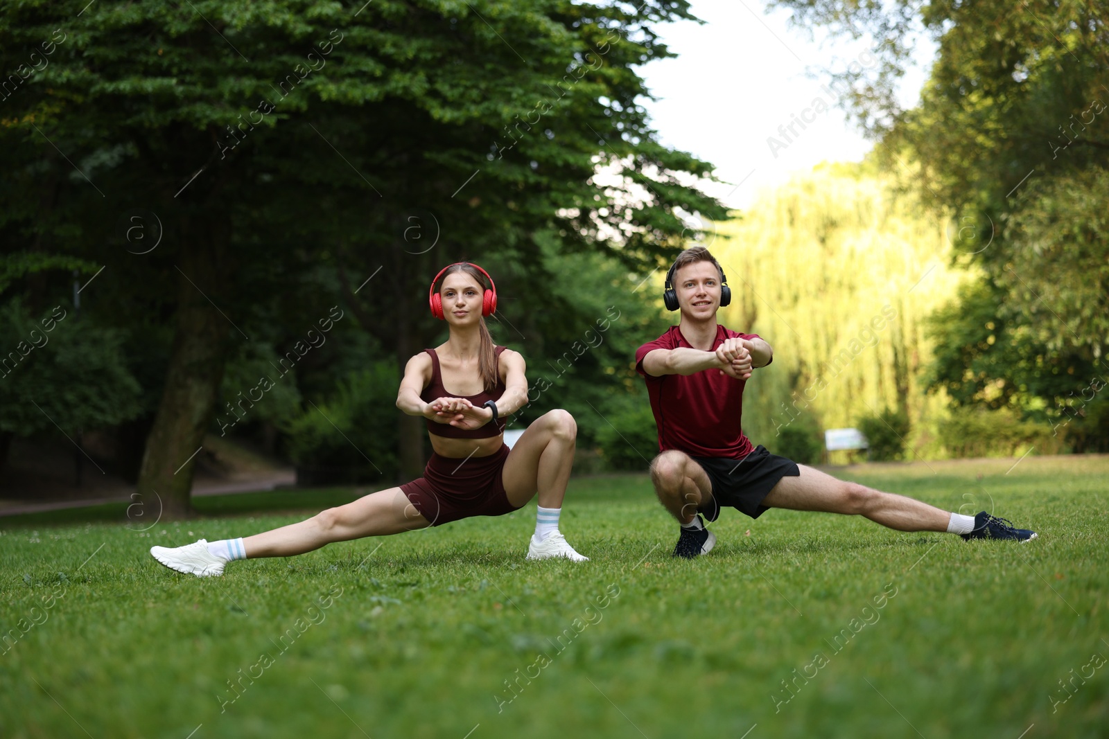 Happy couple in headphones doing morning exercises in park Photo of Happy couple in headphones doing morning exercises in park