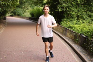 Photo of Smiling sportsman in headphones running outdoors. Morning exercise