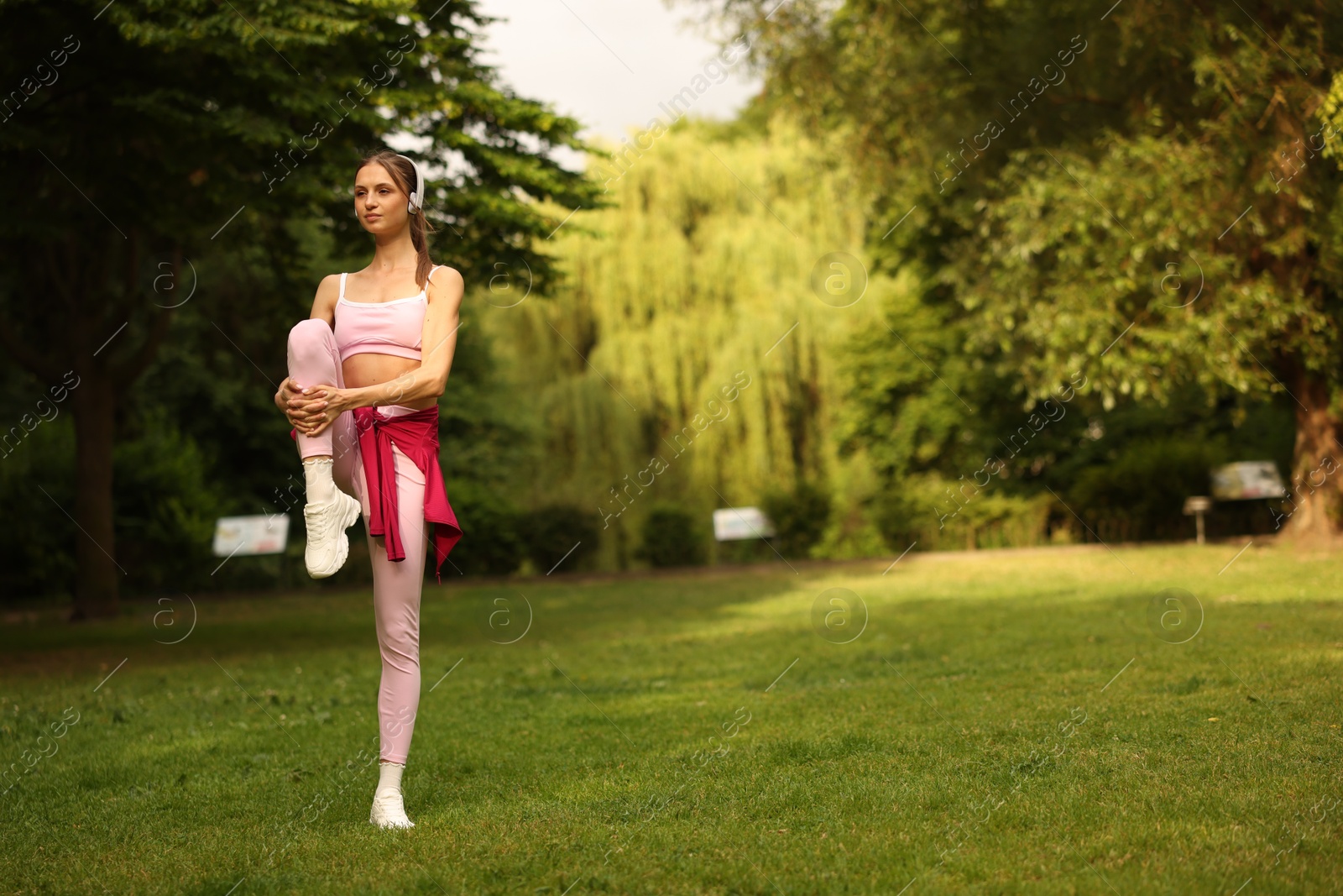 Young sportswoman in headphones doing morning exercise in park. Space for text Photo of Young sportswoman in headphones doing morning exercise in park. Space for text