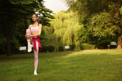Photo of Young sportswoman in headphones doing morning exercise in park. Space for text