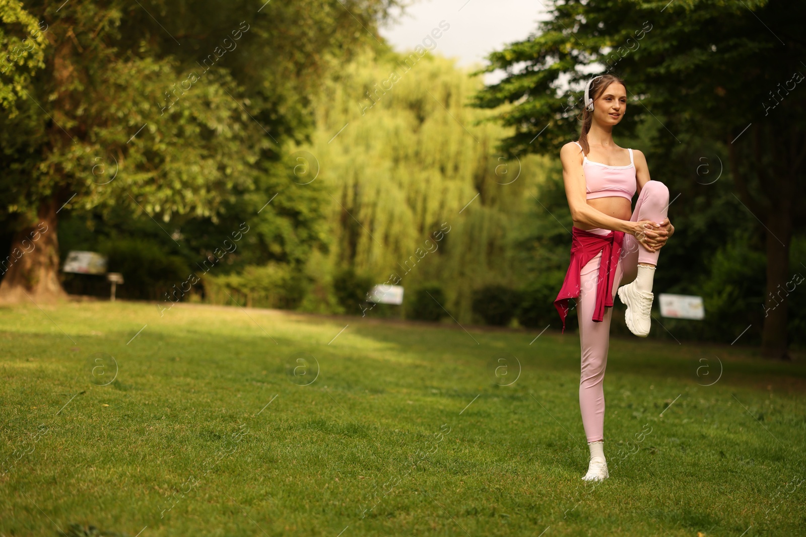 Young sportswoman in headphones doing morning exercise in park. Space for text Photo of Young sportswoman in headphones doing morning exercise in park. Space for text