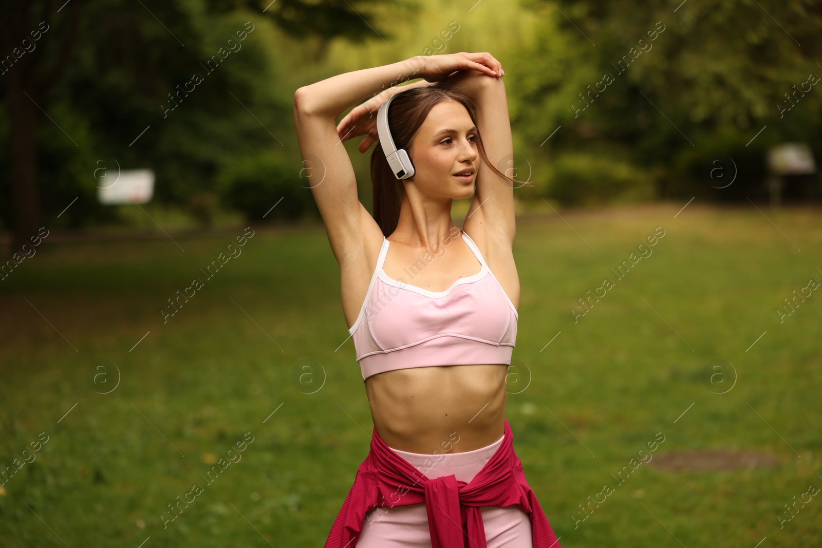 Young sportswoman in headphones doing morning exercise in park Photo of Young sportswoman in headphones doing morning exercise in park