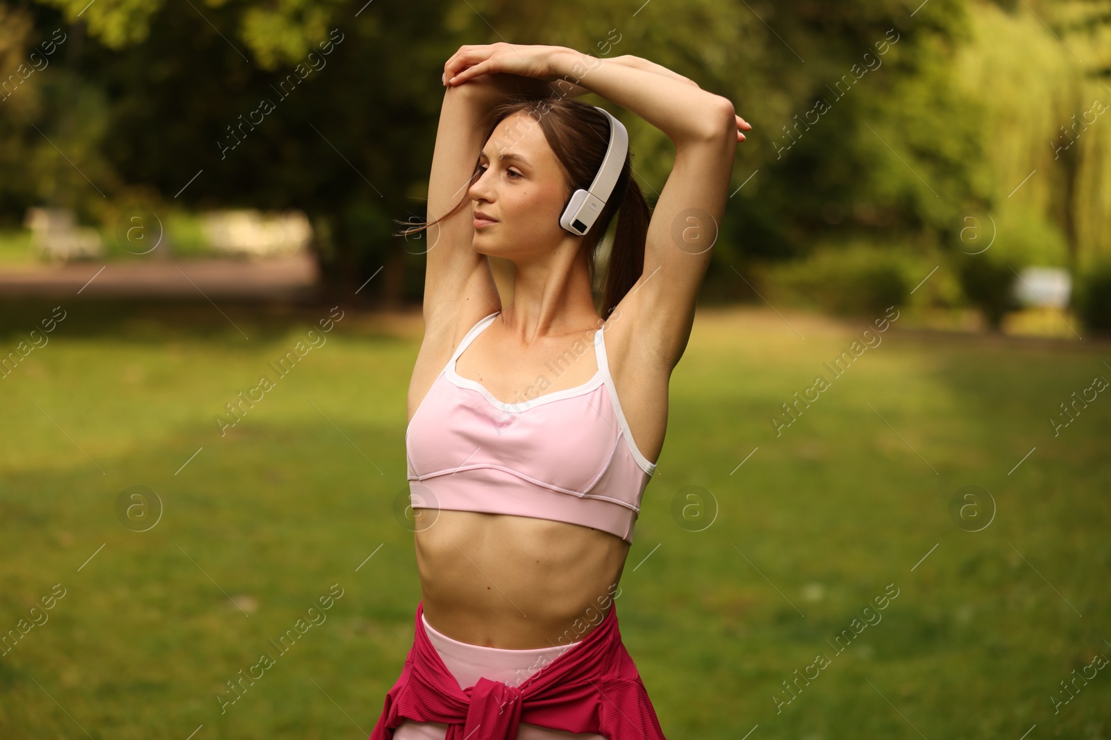 Young sportswoman in headphones doing morning exercise in park Photo of Young sportswoman in headphones doing morning exercise in park
