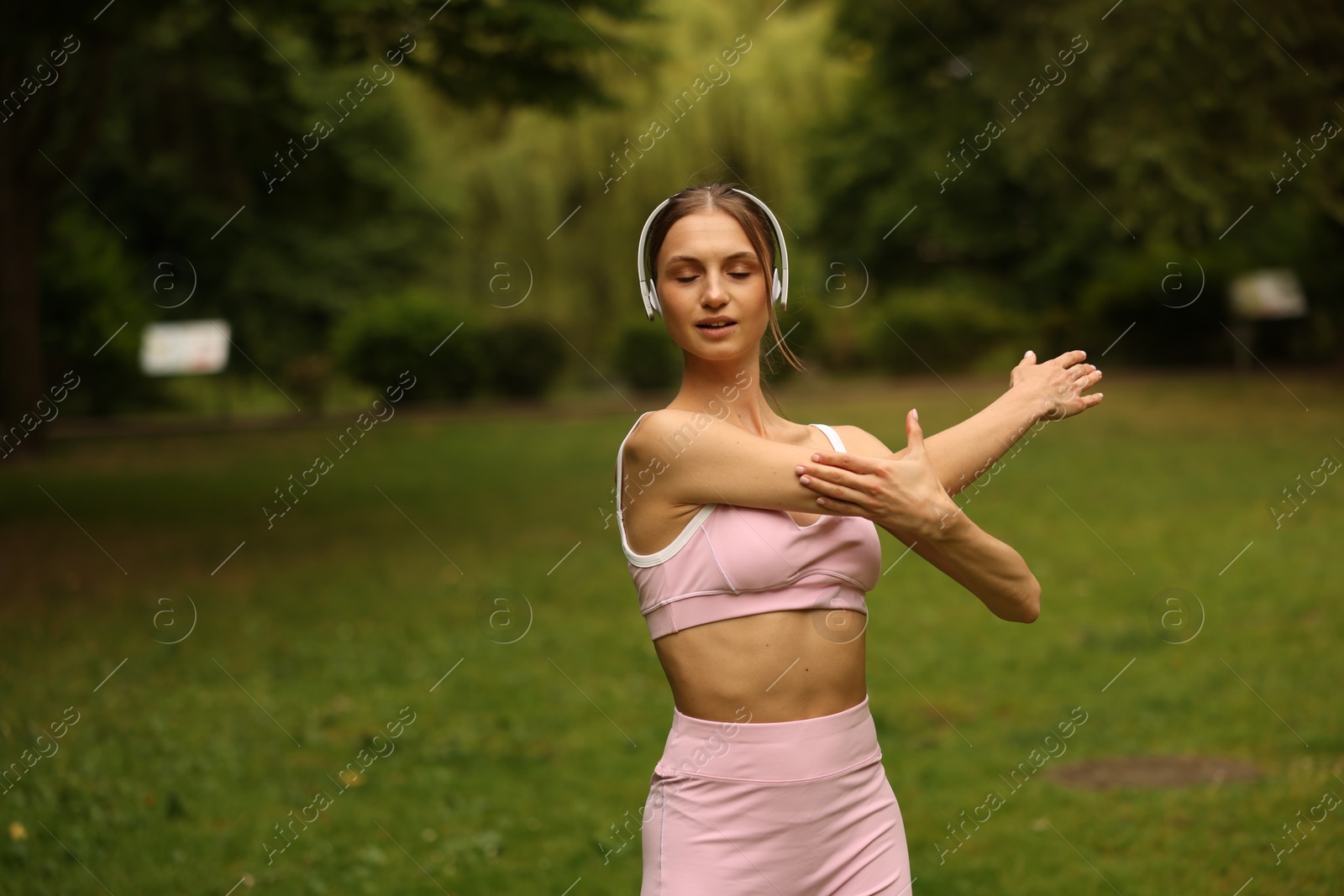 Young sportswoman in headphones doing morning exercise in park Photo of Young sportswoman in headphones doing morning exercise in park