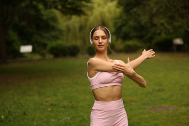 Photo of Young sportswoman in headphones doing morning exercise in park