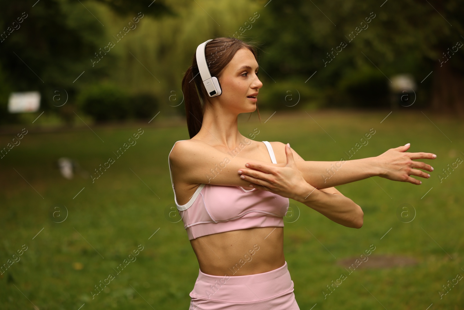 Young sportswoman in headphones doing morning exercise in park Photo of Young sportswoman in headphones doing morning exercise in park