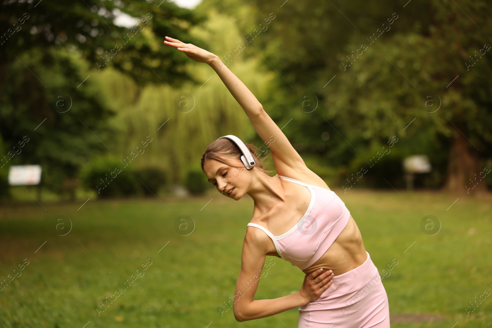 Young sportswoman in headphones doing morning exercise in park Photo of Young sportswoman in headphones doing morning exercise in park