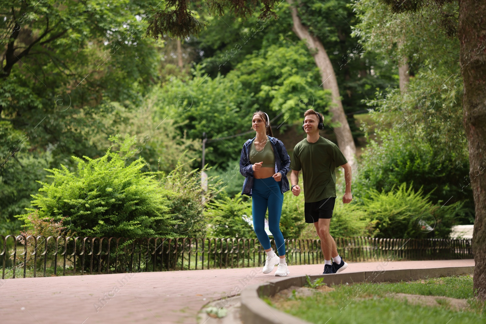 Happy couple in headphones running in park, low angle view. Morning exercise Photo of Happy couple in headphones running in park, low angle view. Morning exercise