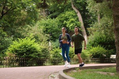 Photo of Happy couple in headphones running in park, low angle view. Morning exercise