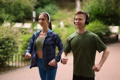 Photo of Happy couple in headphones running in park. Morning exercise