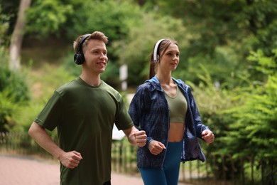 Photo of Happy couple in headphones running in park. Morning exercise