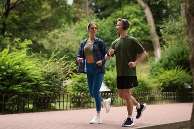 Photo of Happy couple in headphones running in park, low angle view. Morning exercise