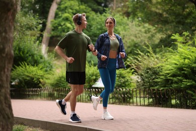 Photo of Happy couple in headphones running in park, low angle view. Morning exercise