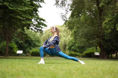Photo of Young sportswoman in headphones doing morning exercise in park
