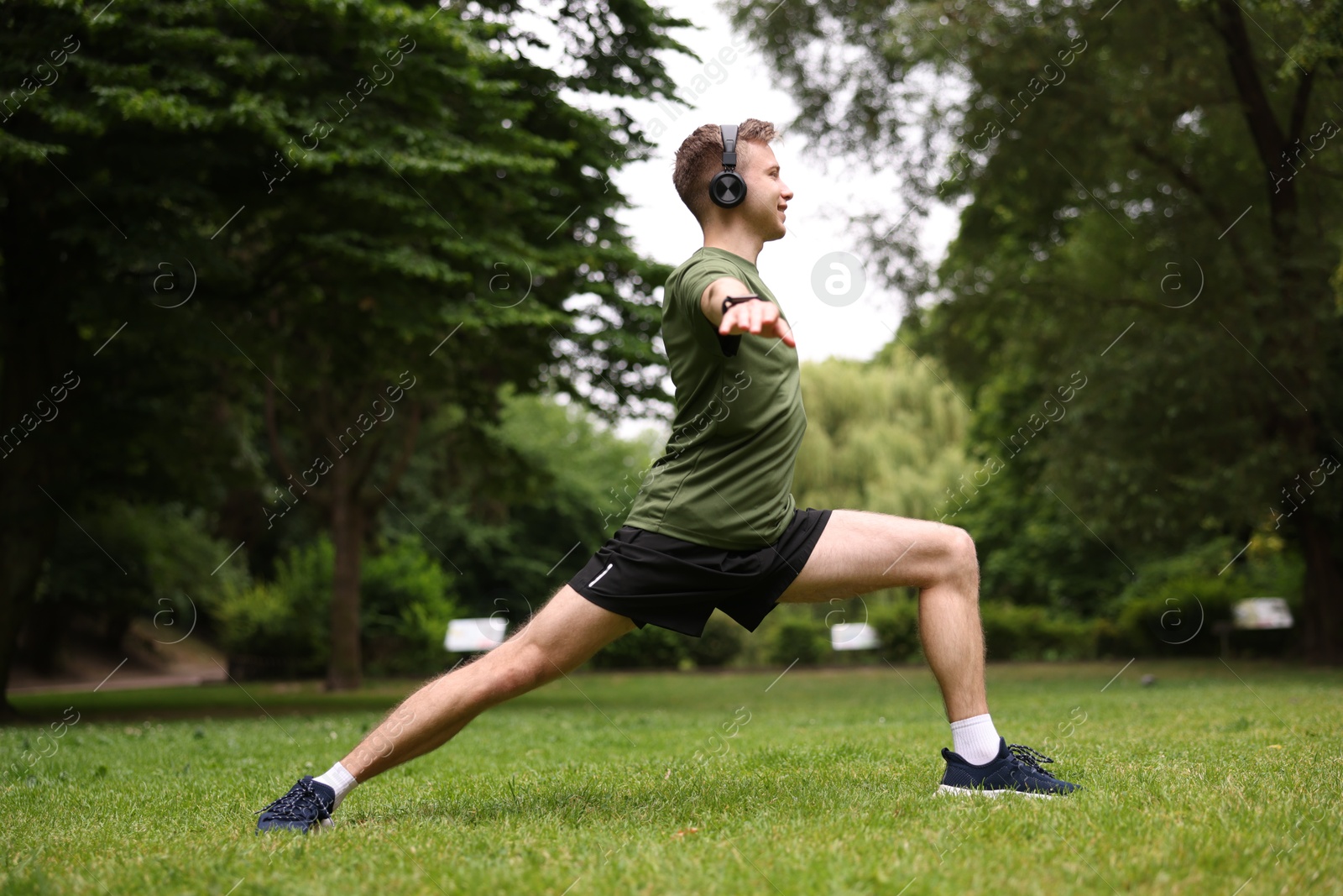 Smiling sportsman in headphones doing morning exercise in park Photo of Smiling sportsman in headphones doing morning exercise in park