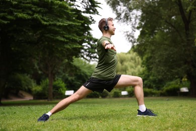 Photo of Smiling sportsman in headphones doing morning exercise in park