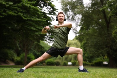 Photo of Smiling sportsman in headphones doing morning exercise in park, low angle view