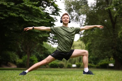 Photo of Smiling sportsman in headphones doing morning exercise in park, low angle view