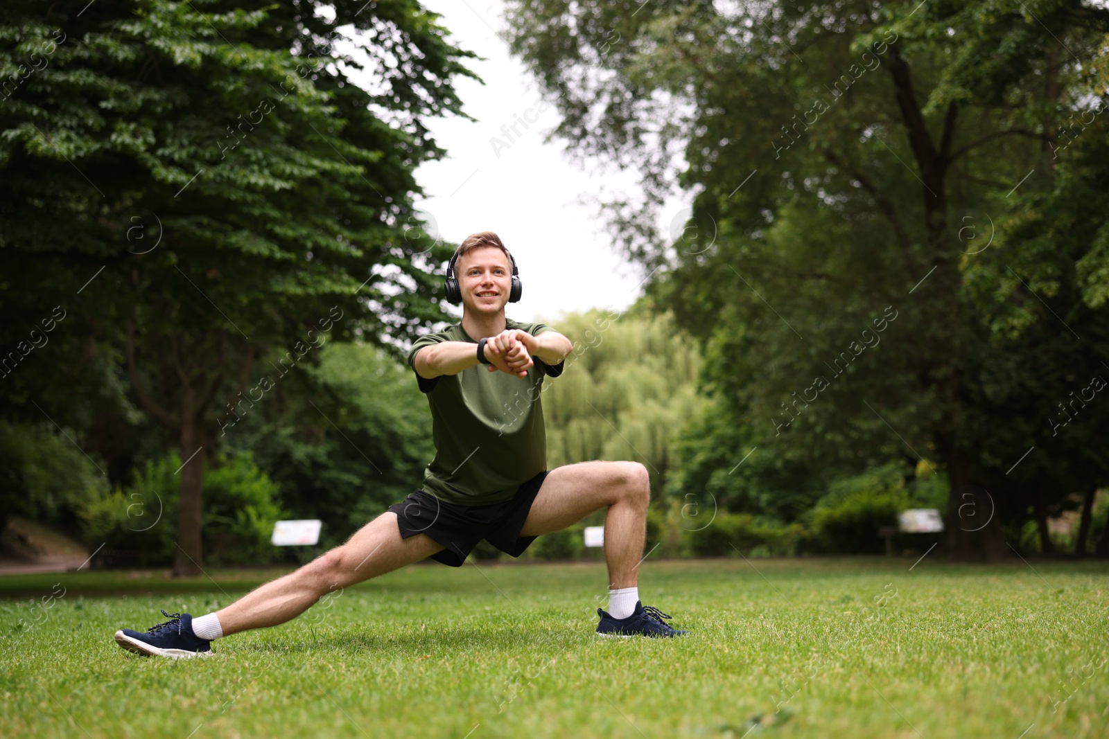 Smiling sportsman in headphones doing morning exercise in park. Space for text Photo of Smiling sportsman in headphones doing morning exercise in park. Space for text