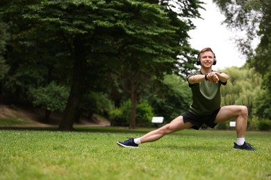 Photo of Smiling sportsman in headphones doing morning exercise in park. Space for text
