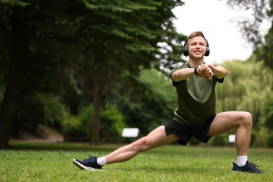 Photo of Smiling sportsman in headphones doing morning exercise in park. Space for text