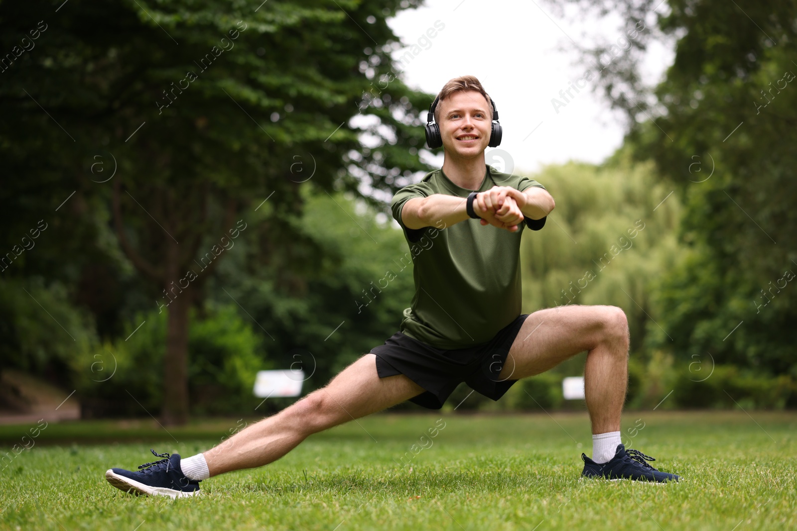 Smiling sportsman in headphones doing morning exercise in park Photo of Smiling sportsman in headphones doing morning exercise in park