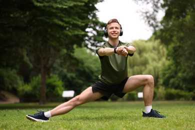 Photo of Smiling sportsman in headphones doing morning exercise in park
