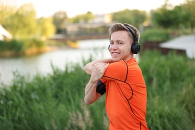 Photo of Smiling sportsman in headphones doing morning exercise outdoors