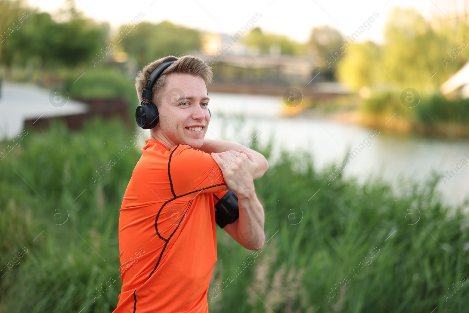 Smiling sportsman in headphones doing morning exercise outdoors Photo of Smiling sportsman in headphones doing morning exercise outdoors