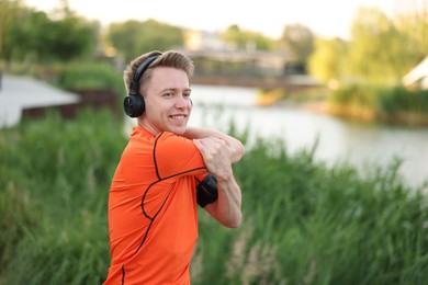 Photo of Smiling sportsman in headphones doing morning exercise outdoors