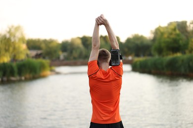 Photo of Sportsman in armband doing morning exercise near river, back view